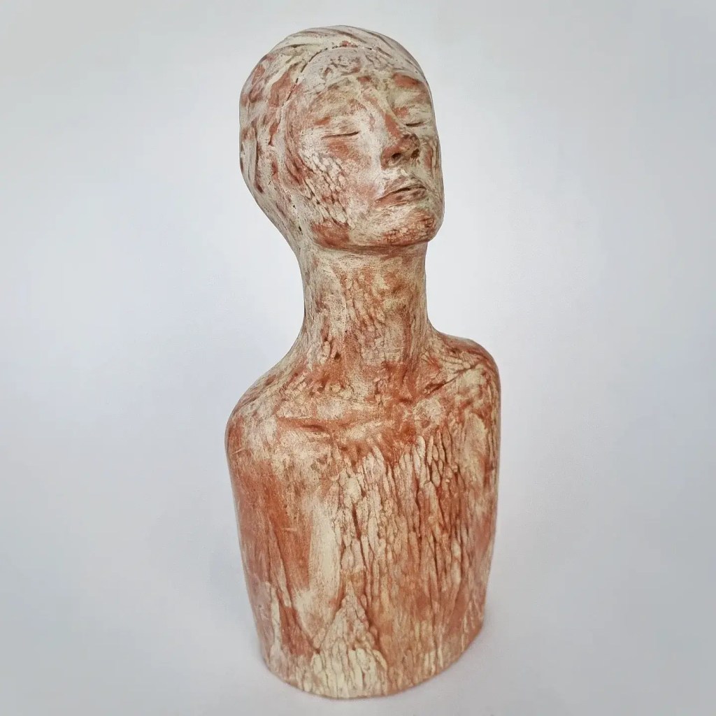 Ceramic figurative sculpture of woman praying in terracotta and pale yellow on white background, front view.