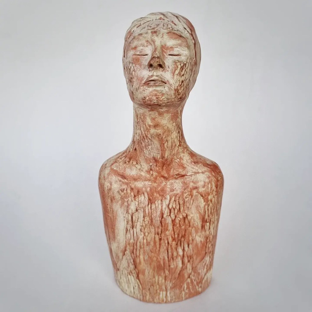 Ceramic figurative sculpture of woman praying in terracotta and pale yellow with textures on white background