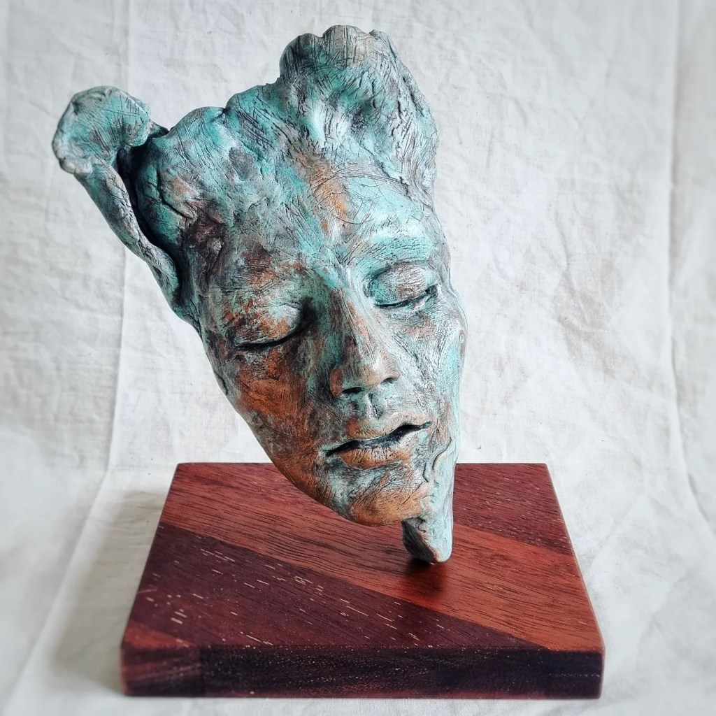 Abstract blue ceramic face sculpture balancing on wooden base