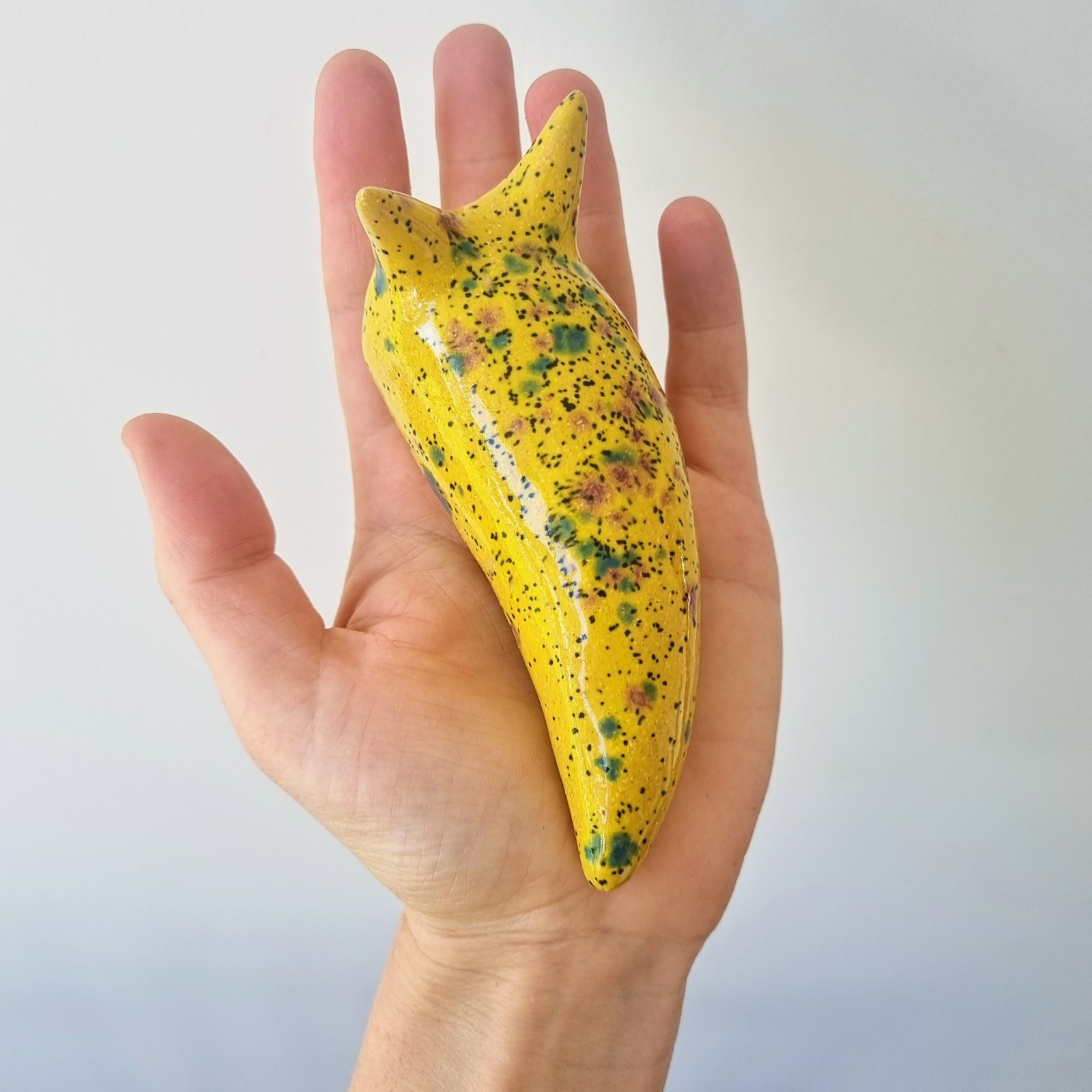 Hand holding yellow ceramic slug. Karen Wilde New Zealand Contemporary Ceramic Sculpture Artist