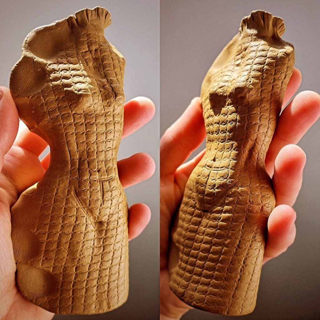 A hand holding a clay sculpture resembling a textured dress form, showcasing intricate woven patterns and an earthy appearance.